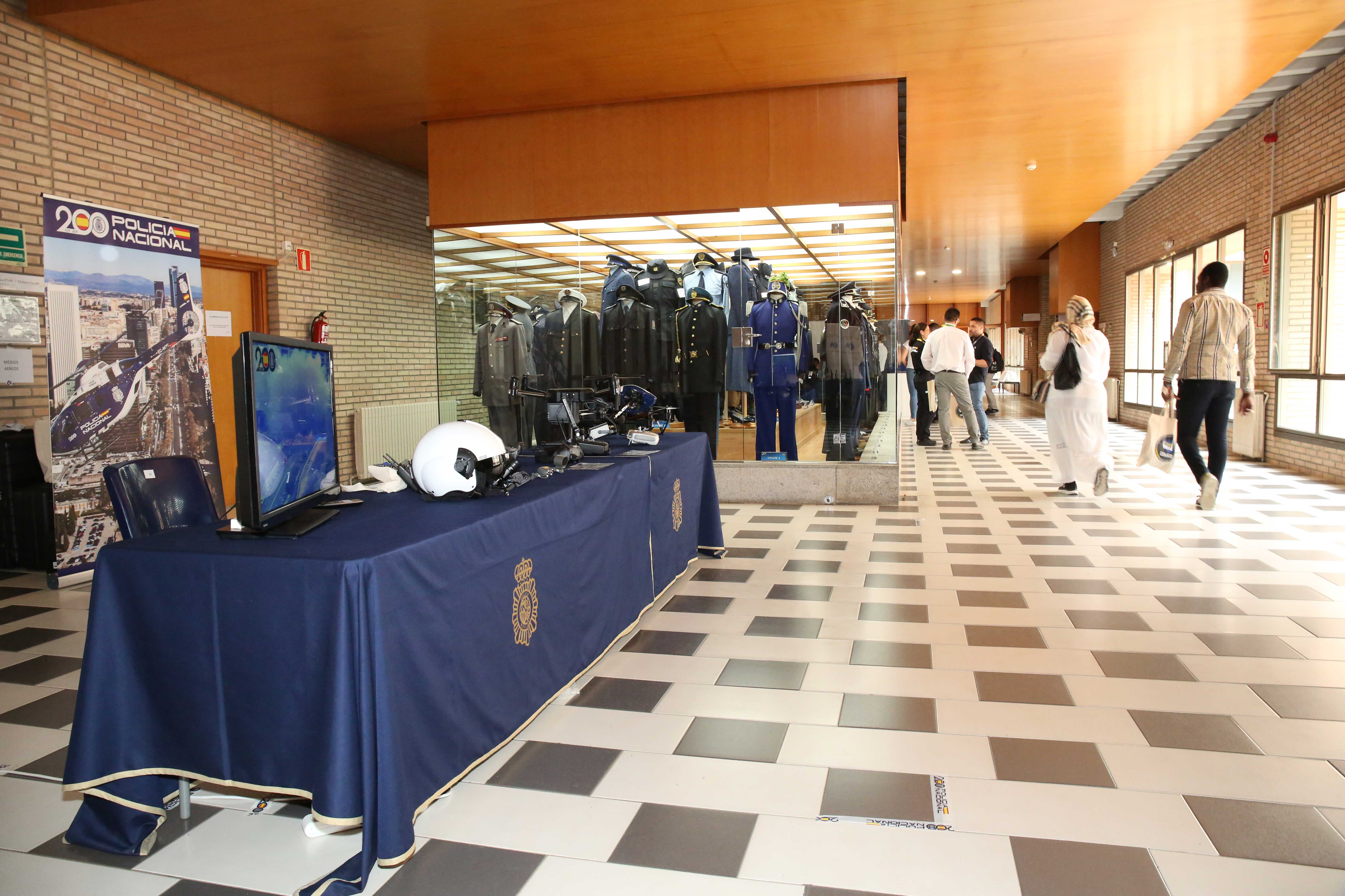 Fotografía de un pasillo de la Escuela Nacional de Policía mostrando material de la Unidad de Medios Aéreos junto a una exposición de trajes de policías de otros paises.