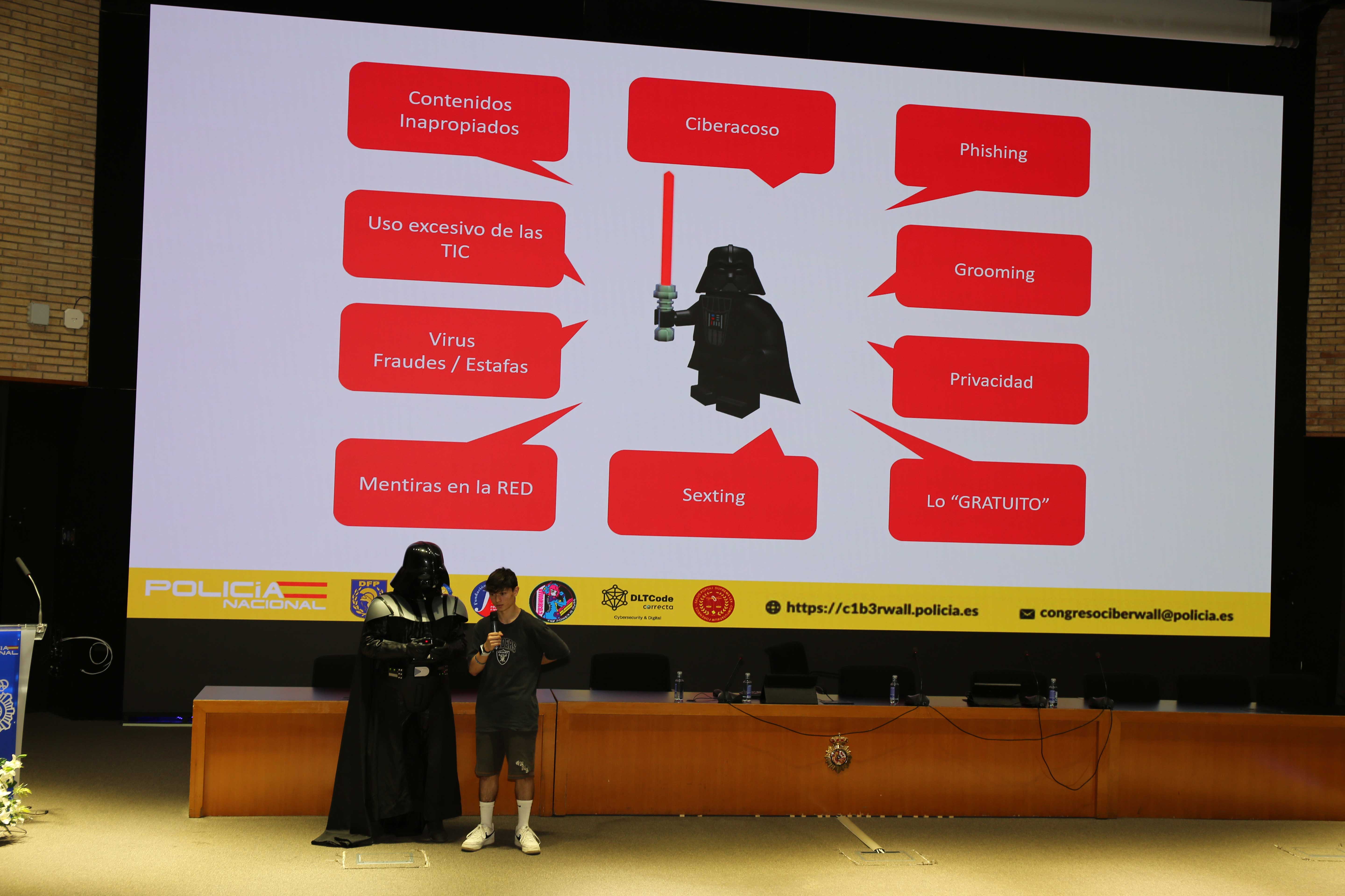 Fotografía de una persona disfrazado de Darth Vader dando una conferencia a jóvenes en el congreso C1b3rWall 2025.